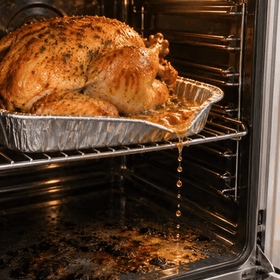 Turkey juices dripping from a foil pan onto the oven floor